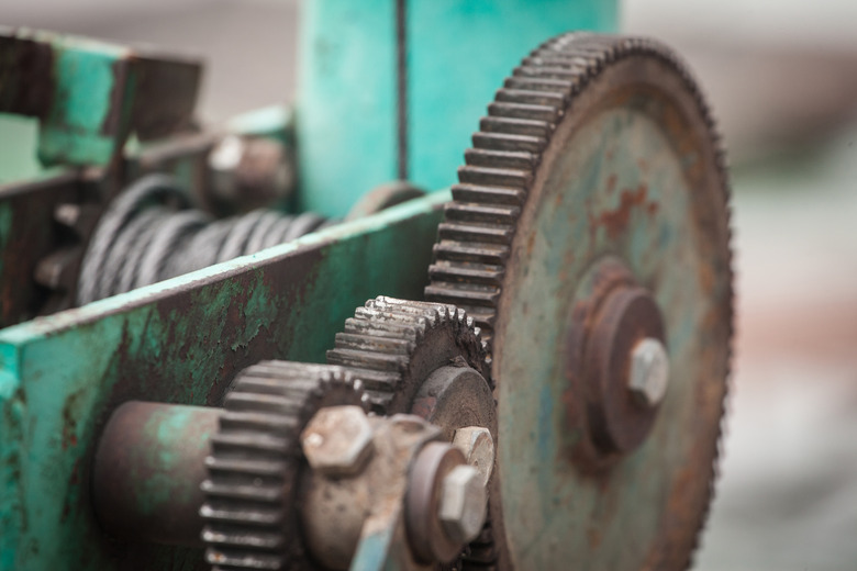 Selective blur on cogwheels and gear in a green metal industrial machinery device used to demultiply power and force.