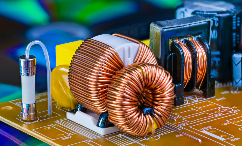 Toroidal inductor with copper wire winding, transformer and electric fuse. Detail of induction coil with magnetic ferrite core. Inverter. Current safeguard