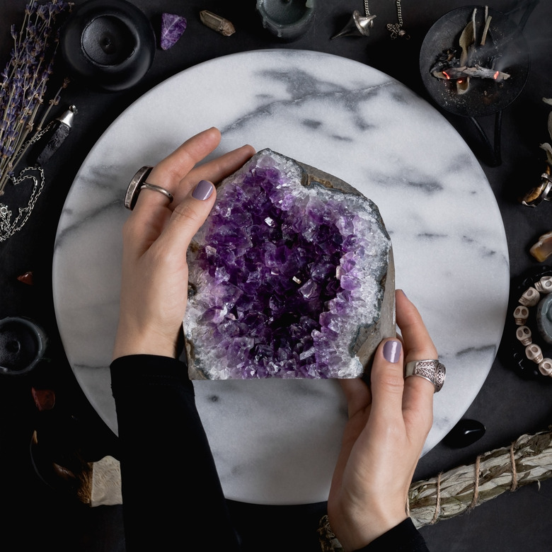 The witch is holding amethyst stone surrounded magic things. View from above.