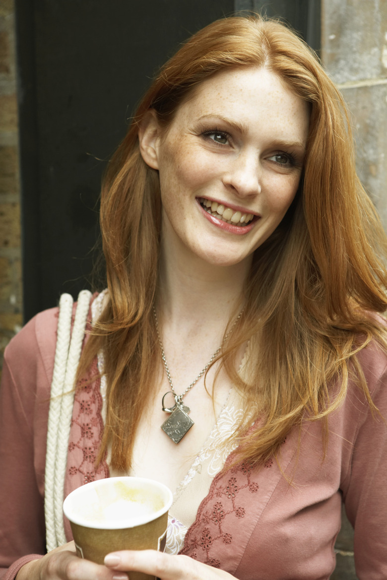 Young woman holding disposable cup, looking away, smiling