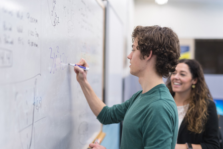 Ethnic teacher helps high school student with a math problem on the whiteboard