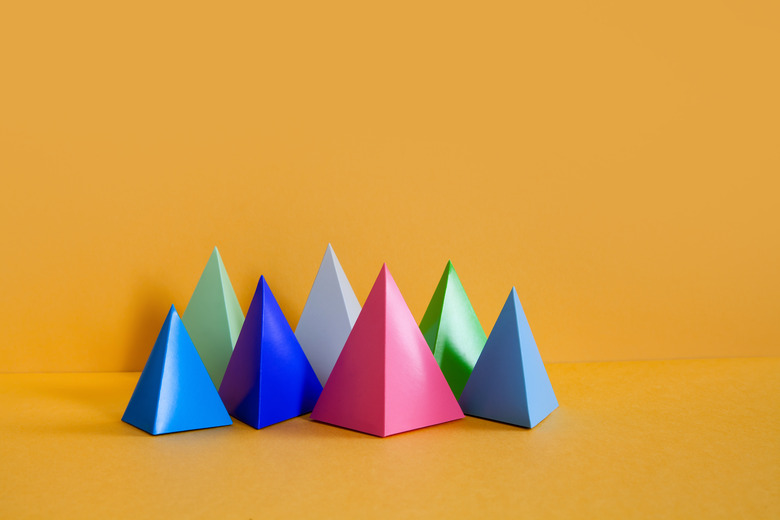 Minimalist design colorful abstract geometrical composition. Three-dimensional prism pyramid rectangular objects on yellow paper background. Gray blue pink green colored solid figures, soft focus