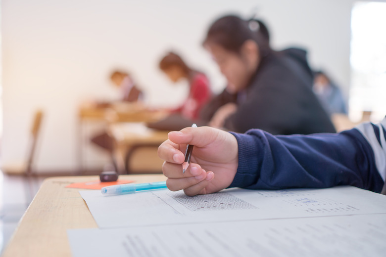 Exams test student in high school, university student holding pencil for testing exam writing answer sheet and exercise for taking in assessment paper on wood table classroom. Education study Concept