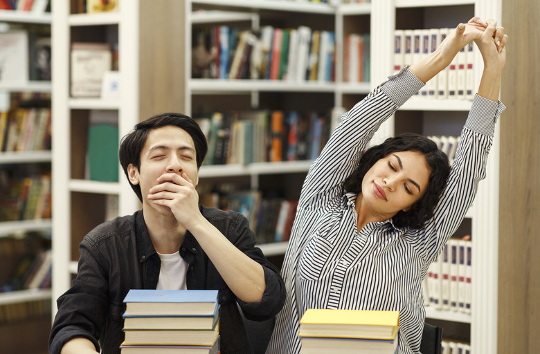 Tired students yawning and stretching in the campus library