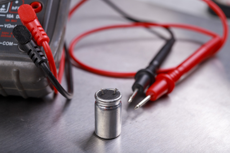 Capacitor and electrical meter. Measurement work in an electrical workshop. Metallic background.