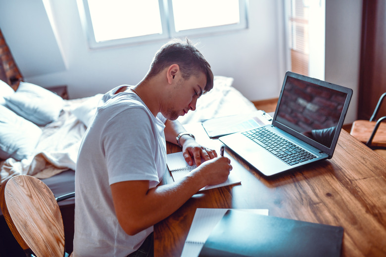 Young Male Writing Homework Before Online Lesson