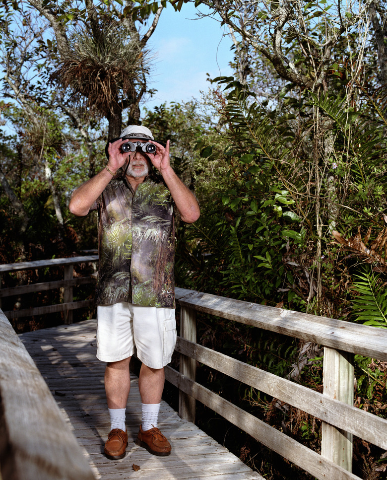 Senior man looking through binoculars on wooden walkway