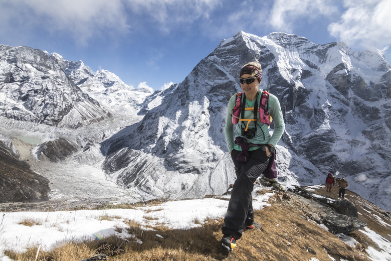 A young woman ascends a grassy ridge, Himalayan giants in background