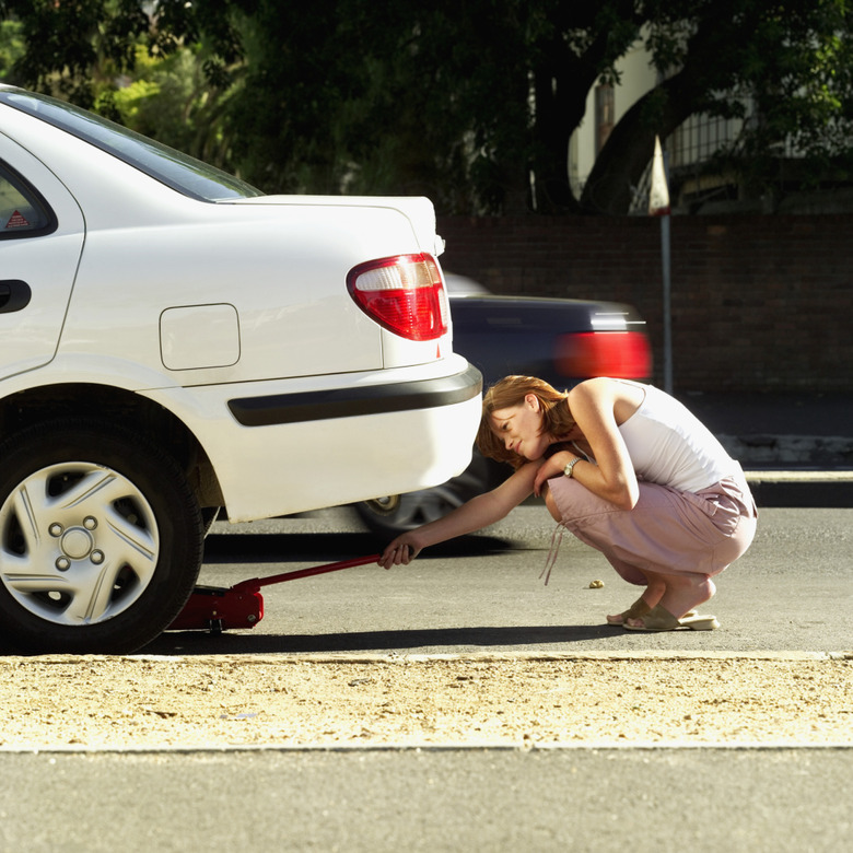 Young woman adjusting jack under a car