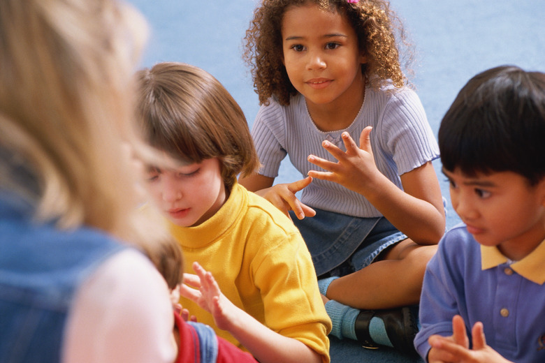 Children sitting listening to teacher and counting on fingers