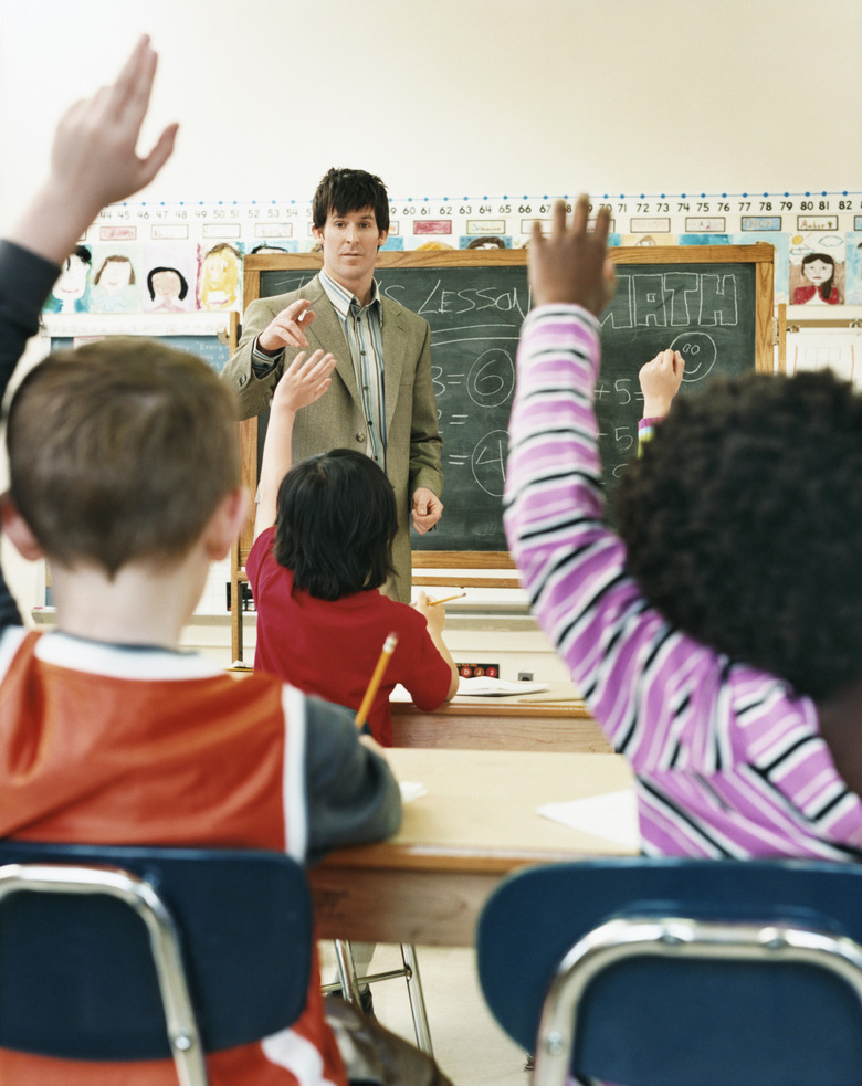 Teacher Pointing to Primary School Students With Raised Hands in a Classroom