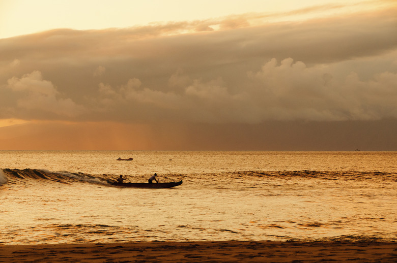 Two men paddling a Hawaiian outrigger canoe at sunset.