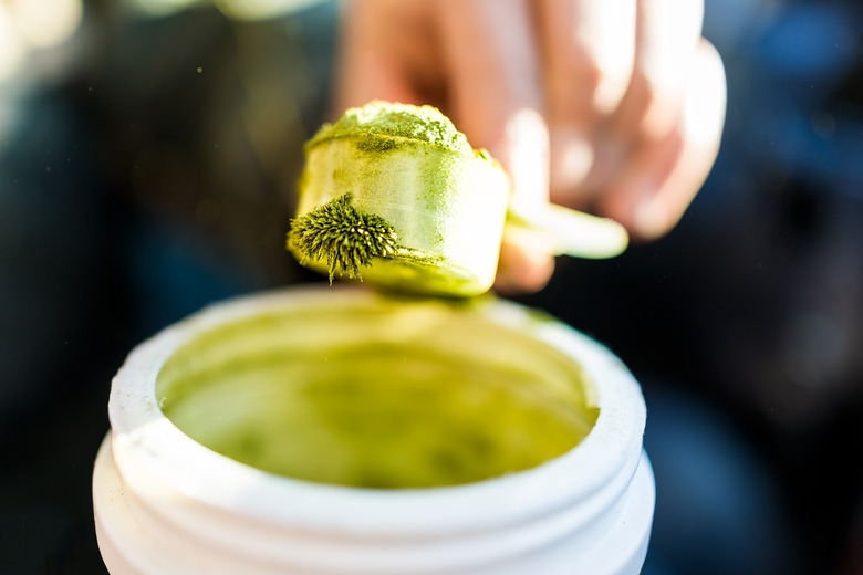 Closeup of wheatgrass powder crystals with static magnetic cling structure on spoon macro with jar, objects attracted to magnets