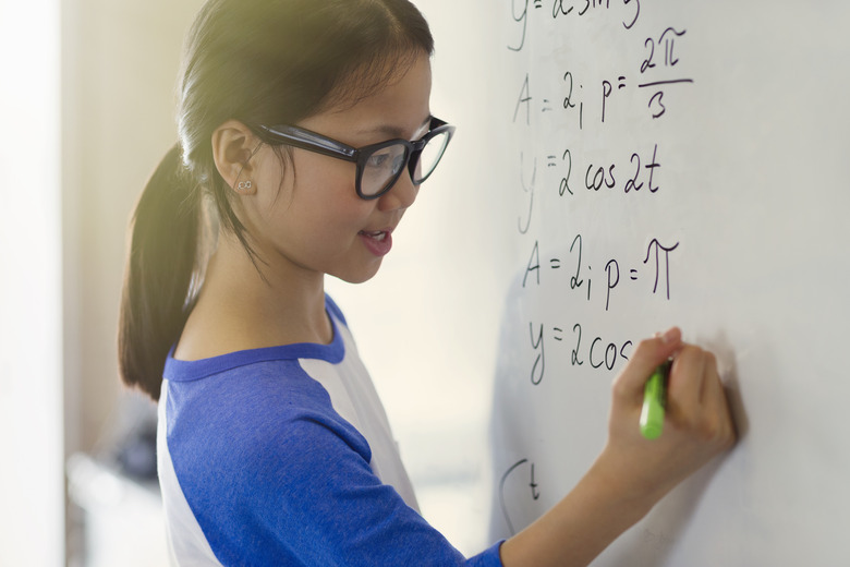 Portrait smiling, confident girl student solving physics equations at whiteboard in classroom