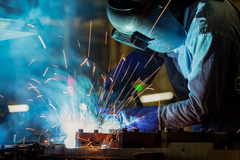 Worker at the factory is welding assembly automotive part