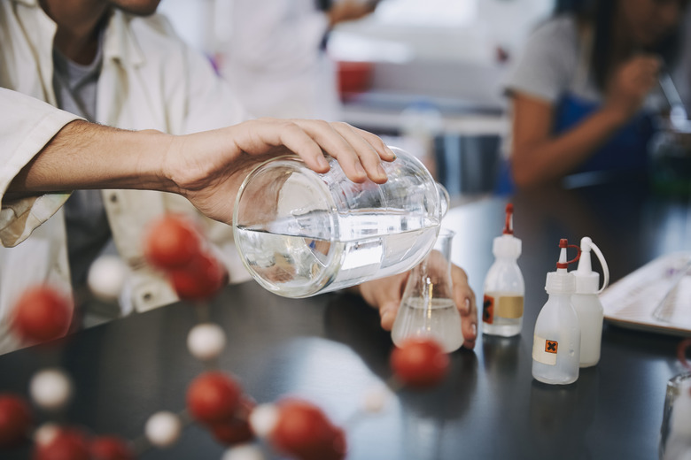 Midsection of young male student pouring liquid solution in flask on table at laboratory