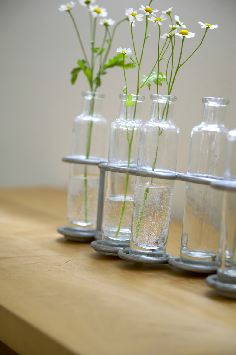 Feverfew flowers (Tanacetum parthenium) in antique glass bottle vases on wooden table