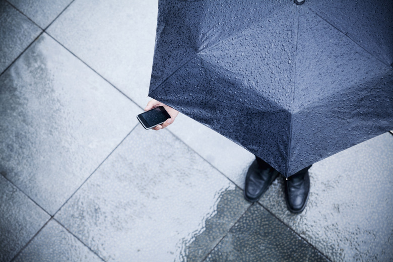 High angle view of businessman holding an umbrella and looking at his phone in the rain