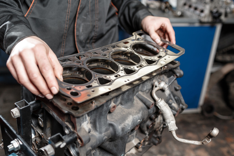 Sealing gasket in hand. The mechanic disassemble block engine vehicle. Engine on a repair stand with piston and connecting rod of automotive technology. Interior of a car repair shop.