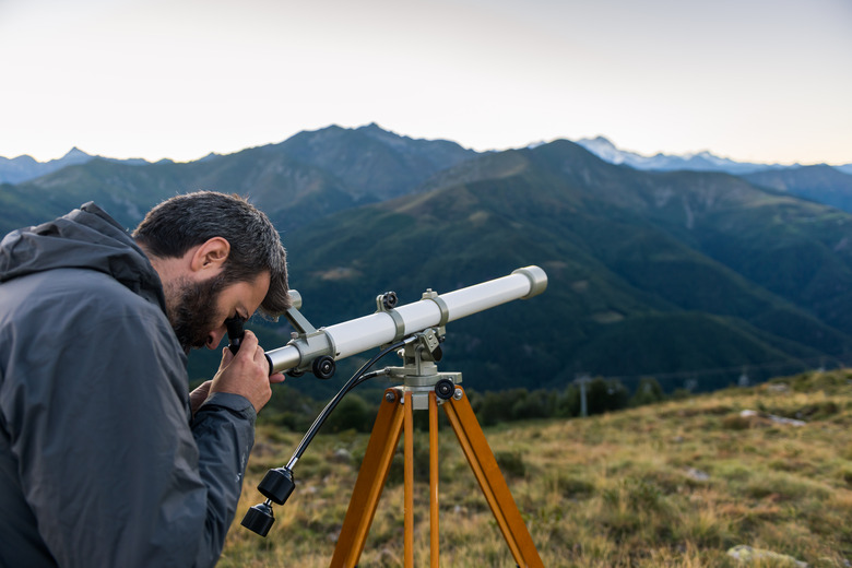 Man looking through telescope mountain peaks in summer evening at sunset on mountain outdoor