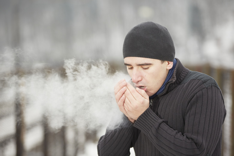 Man in black winter wear warming his hands with his breath