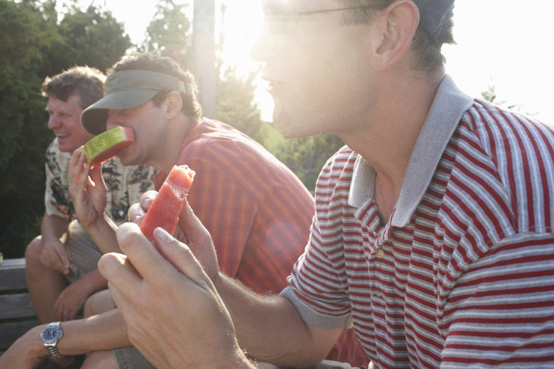 Three men eating watermelon in garden (sun flare)