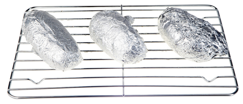 Three baked potatoes in foil on rack