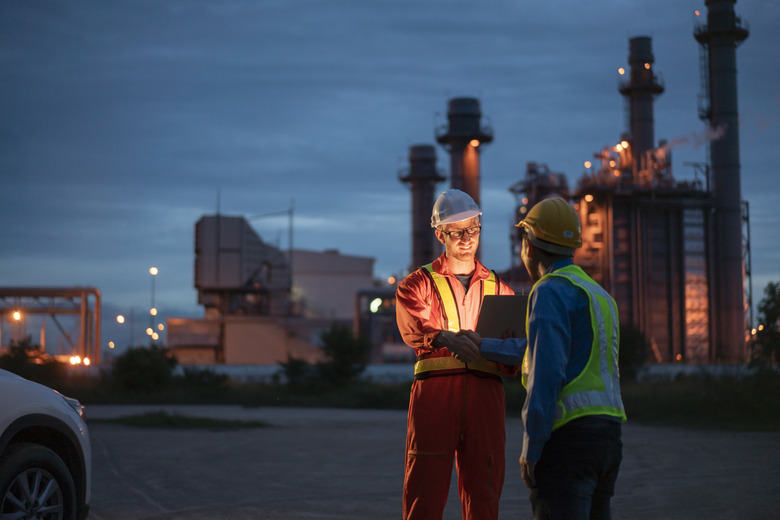 engineer using digital tablet working late night shift at petroleum oil refinery in industrial