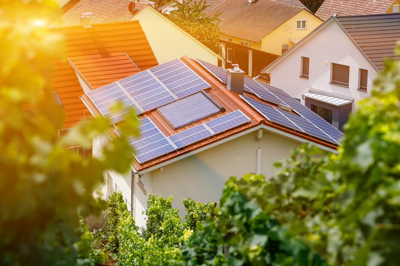 Solar panels on the tiled roof of the building in the sun. Top view through grape leaves. Selective focus.