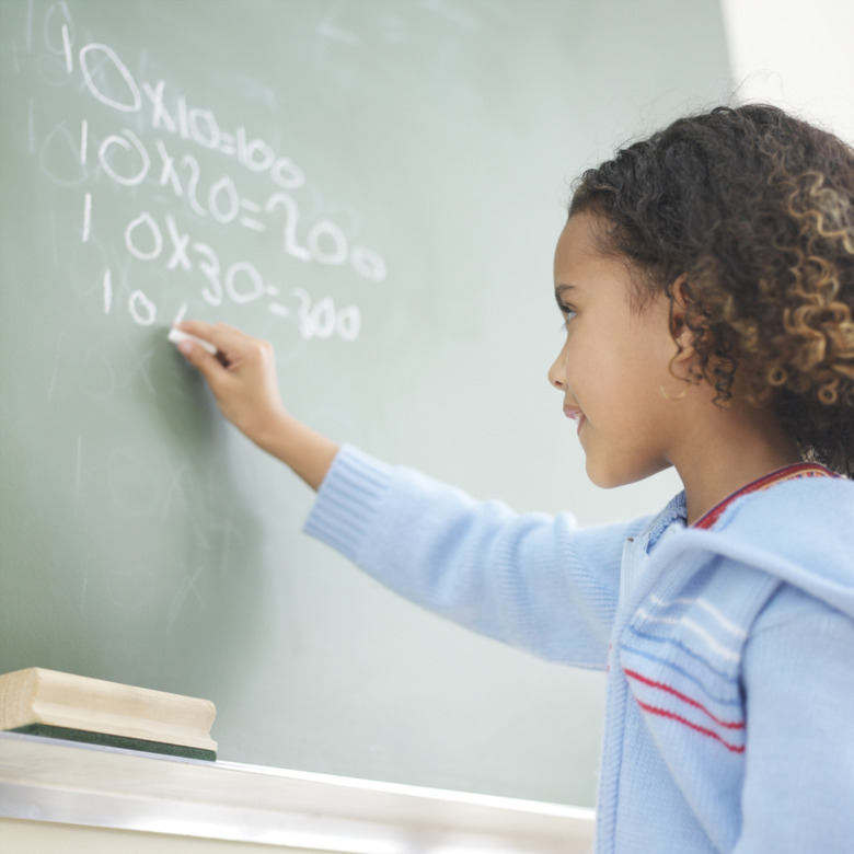 Girl (6-7) writing sums on blackboard, side view