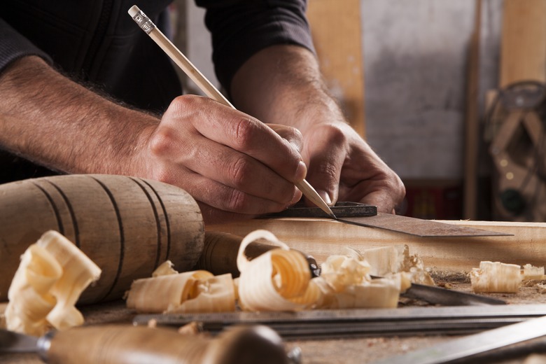 hand of a carpenter taking measurement of a wooden plank