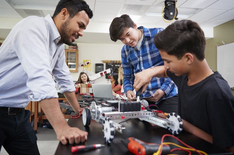 Teacher With Male Pupils Building Robotic Vehicle In Science Lesson