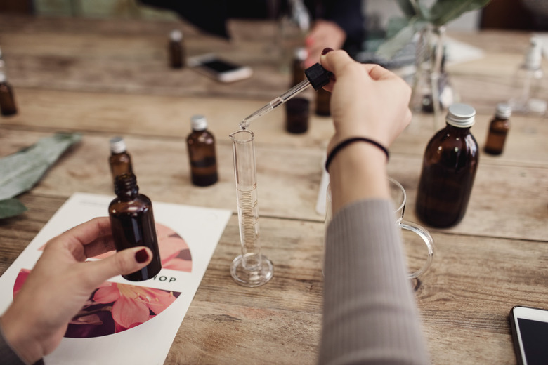 Cropped image of young woman preparing perfume in test tube with pipette at table in workshop