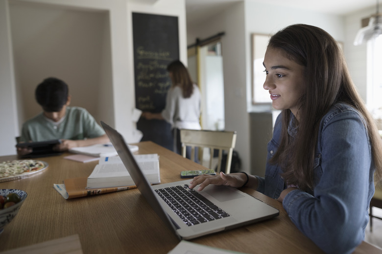 Tween girl doing homework at laptop in kitchen