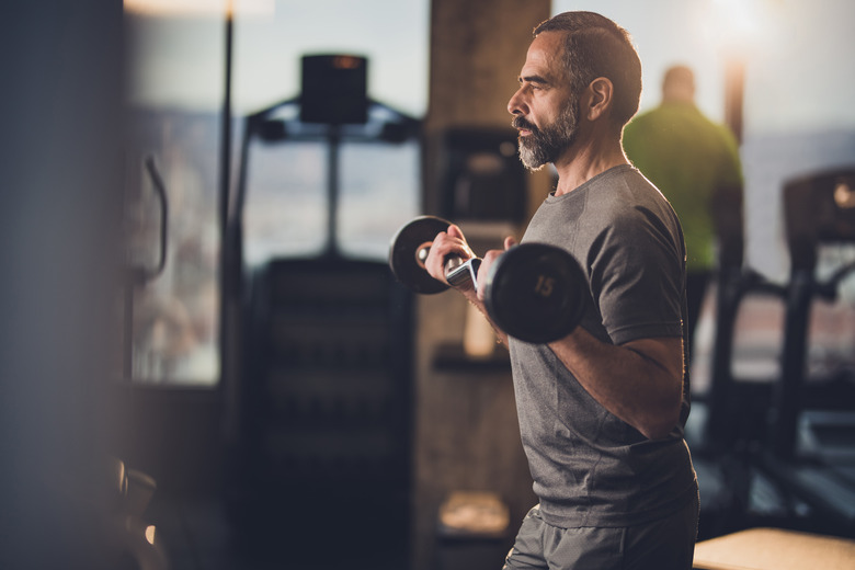 Active senior man having strength exercise with barbell in a gym.