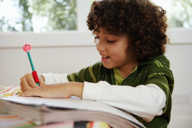 Boy (8-10) doing home-work on bed, smiling