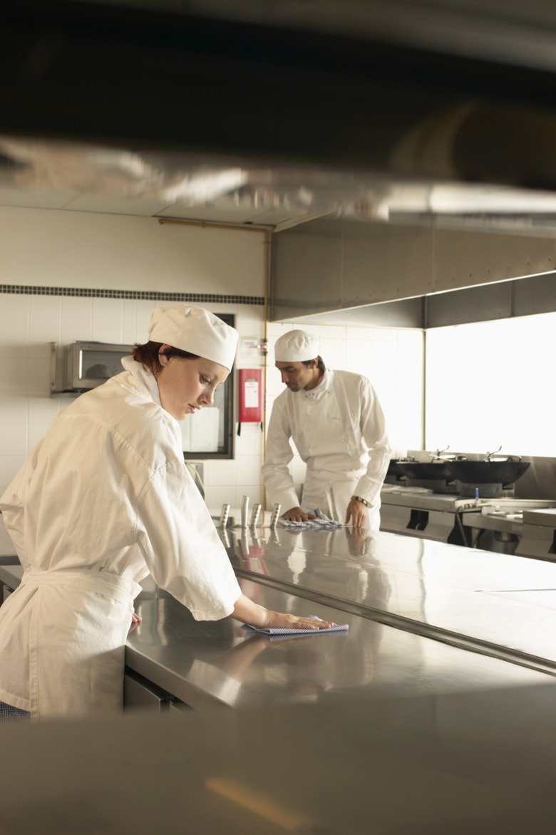 Two male and female cooks members cleaning kitchen surfaces