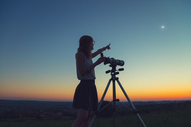 Cute young woman holding astronomical telescope and looking at the sky.