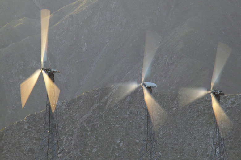 Blurred Motion Shot of Three Wind Turbines Against a Rocky Background