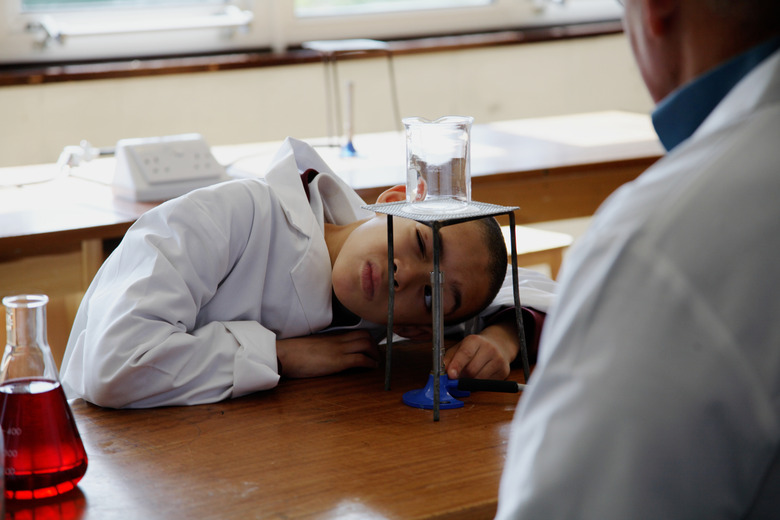 Schoolboy (8-10) in science lesson looking at jar over bunsen burner