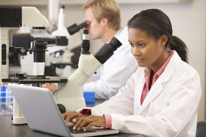 Male And Female Scientists Using Microscopes In Laboratory