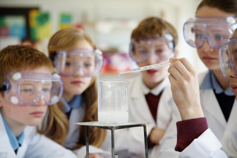 Pupils (11-13) wearing goggles watching experiment in science class