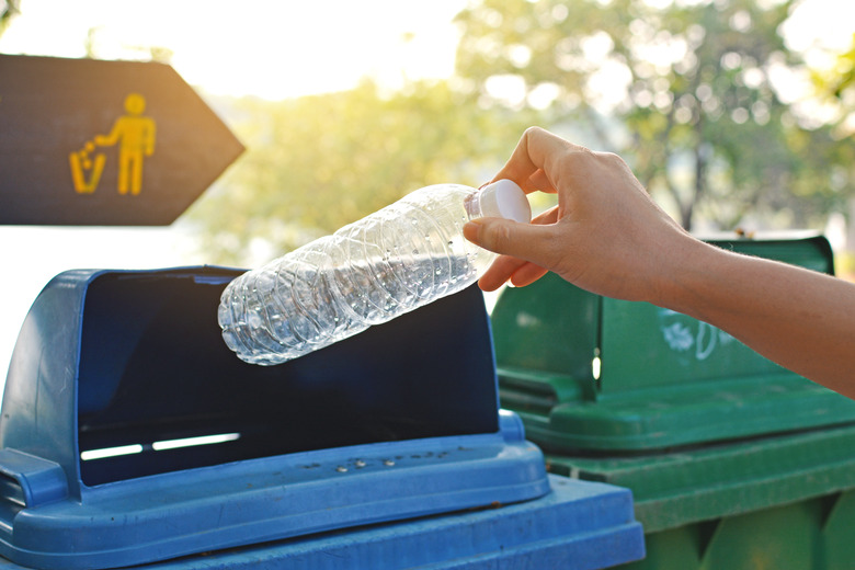 Close-Up Of Hand Throwing Bottle Into Trash Can