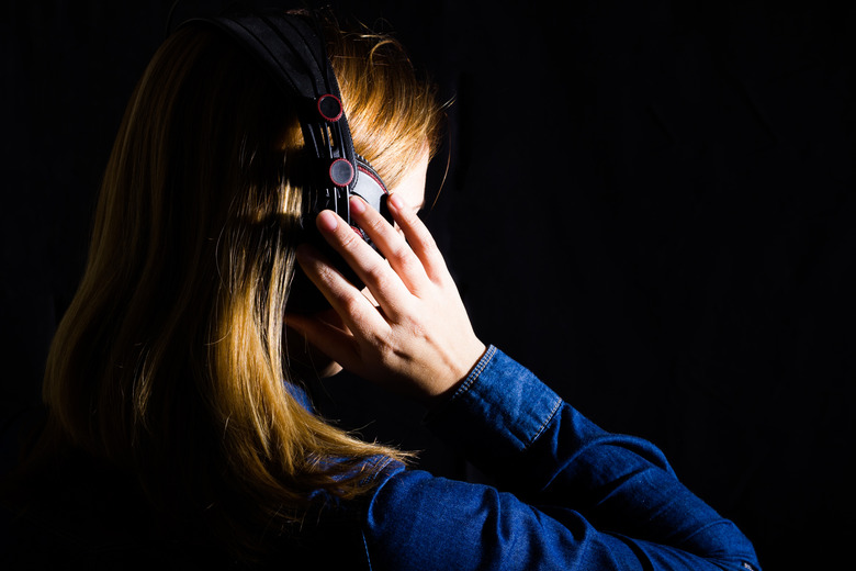 A red haired woman listening to music with headphones on black background and side lighting