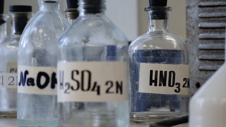 Bottles of solutions stored on shelf in laboratory. Bottles with chemical solutions of NaOH, H2so4 and HNO3. Sulfuric acid, sodium hydroxide, nitric acid