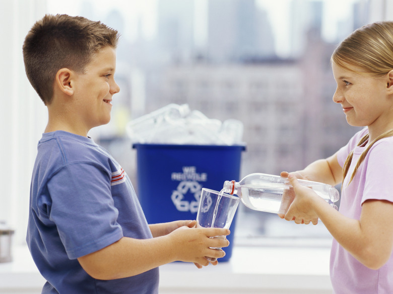 side profile of a sister pouring water into a glass held by her brother