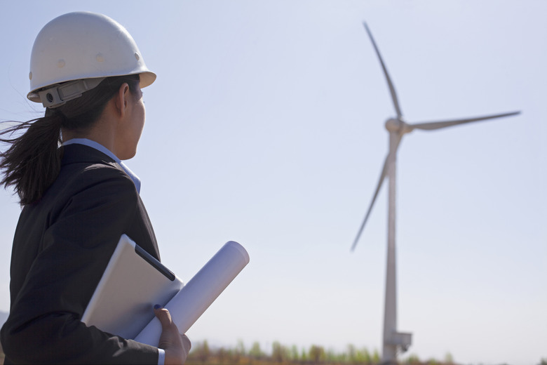 Young female engineer holding blueprints and checking wind turbines on site,