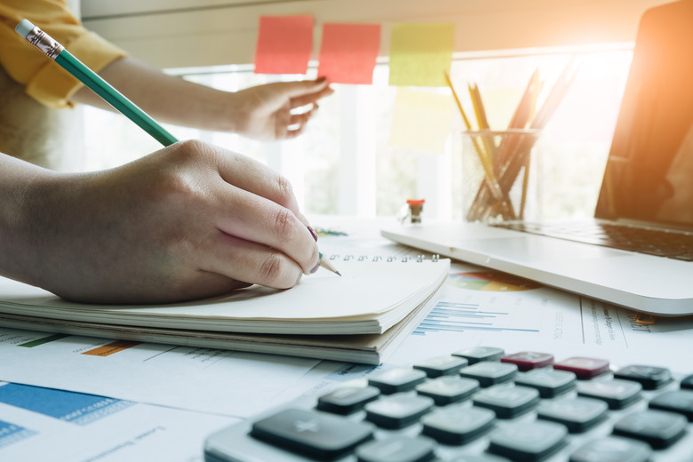 A woman using sticky postit and analysis data report during writing make note some data on notepad, Business financial concept